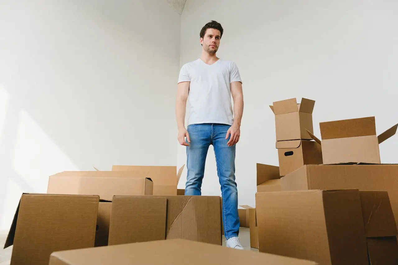 Un homme dépassé debout au milieu des cartons dans une pièce vide lors d'un déménagement